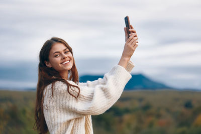 Portrait of young woman with arms raised against sky