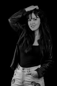 Portrait of young woman standing against black background