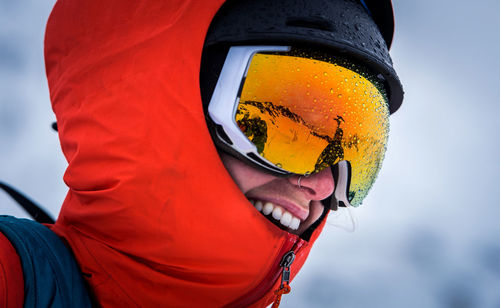 A woman laughing with goggles and a jacket hood on