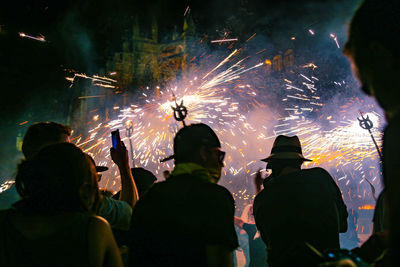 People looking at firework display against sky at night