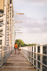 Rear view of people walking on footbridge against sky