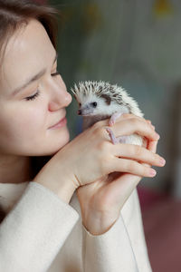 Girl holds cute hedgehog in her hands. portrait of pretty curious muzzle of animal. favorite pets. 