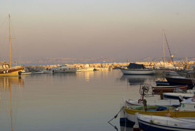 Boats moored in harbor at sunset