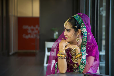  asian woman in a magenta indian tradition sari, she is looking at the side next to the windows