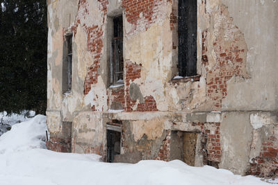Snow covered old building by house during winter