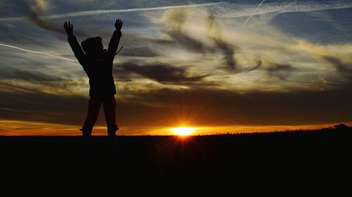 Silhouette person standing on field against sky during sunset
