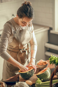 Young woman peels a pumpkin for baking in an apron in the kitchen. the concept of healthy nutrition