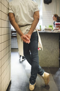 Low section of male chef standing with hands behind back in kitchen at restaurant