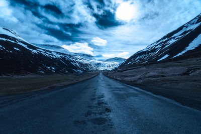 Road amidst mountains against sky during winter