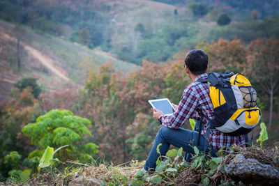 Man using digital tablet while sitting on rock