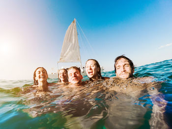 Portrait of friends swimming in sea against blue sky