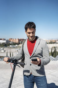 Young man holding camera against clear sky