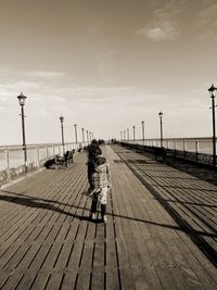 Rear view of woman walking on footpath by street against sky