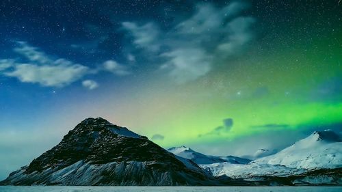 Green aura light, scenic view of snowcapped mountains against sky at night