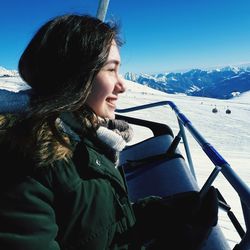 Smiling young woman in ski lift on snowcapped mountain