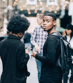 Side view of man holding camera while standing outdoors