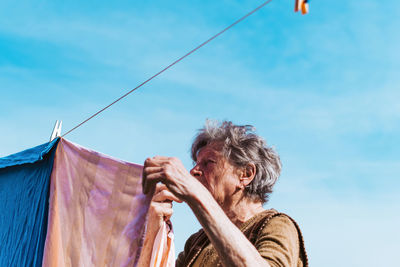 Woman drying laundry on clothesline against blue sky