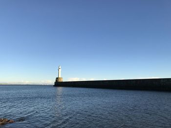 Lighthouse by sea against clear blue sky