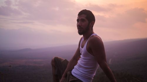 Man sitting on landscape against sky during sunset