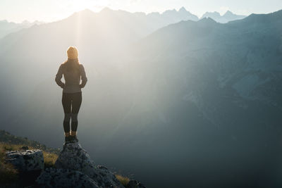 Young woman hiker standing on the edge of cliff at sunrise. backlight sunlight  sunbeam. copy space