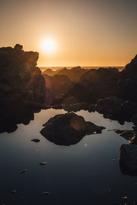 Rocks by lake against sky during sunset