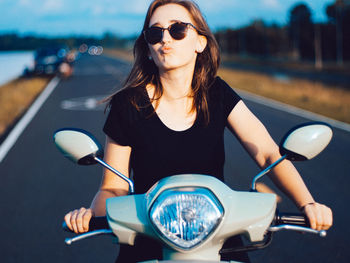 Young woman wearing sunglasses riding motor scooter