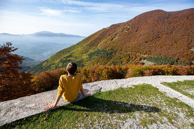 Young woman is sitting and looking at autumn landscape in italy. 