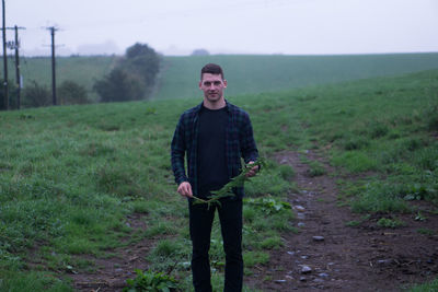 Portrait of young man standing on field against sky