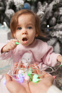 Portrait of cute girl holding christmas lights while sitting at home