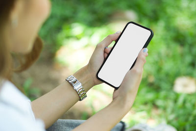 Midsection of woman using mobile phone sitting at park