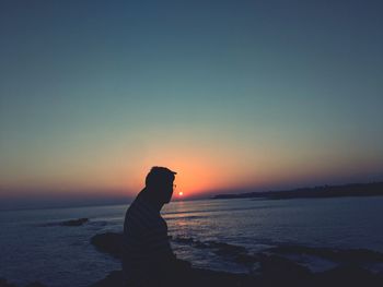 Silhouette man standing at beach against clear sky during sunset