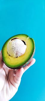 Close-up of hand holding apple against blue background