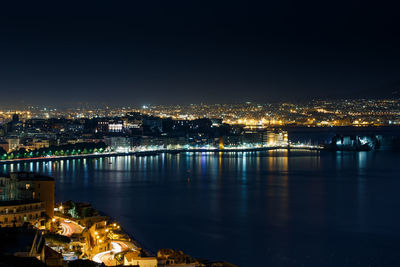 Aerial view of illuminated cityscape by sea against clear sky at night