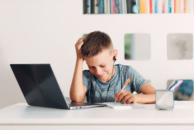 Boy holding pen over book by laptop on table