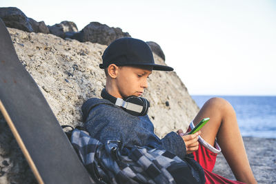 Side view of boy using mobile phone while sitting at beach