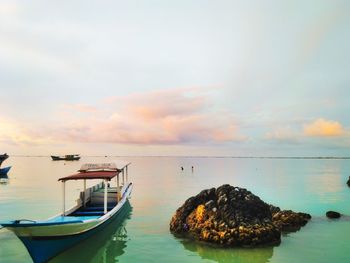 Boats moored in sea against sky during sunset