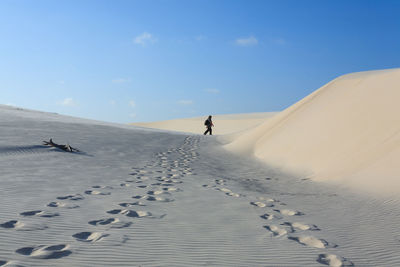 Man walking on sand dunes at desert against sky