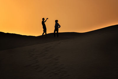 Low angle view of silhouette friends standing at desert against orange sky