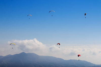 Low angle view of people paragliding against sky