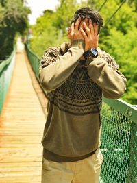 Man covering face while standing on footbridge