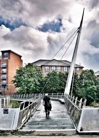 Man walking on bridge in city against sky