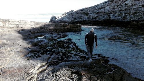 Rear view of man on rock by sea