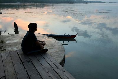 Young man sitting on pier by lake during sunset