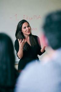 Mid adult woman gesturing while teaching students in language school