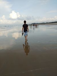 Rear view of man walking on beach against sky