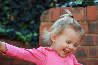 Cheerful girl standing against brick wall at yard