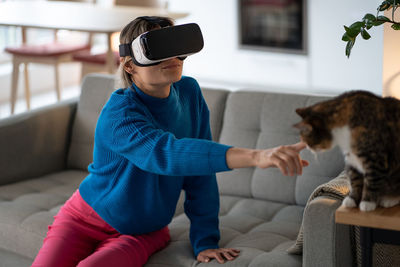 Young woman in vr glasses explores game and tries to touch domestic cat sitting on wooden table