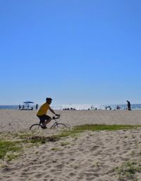 Side view of man riding bicycle at beach against clear sky
