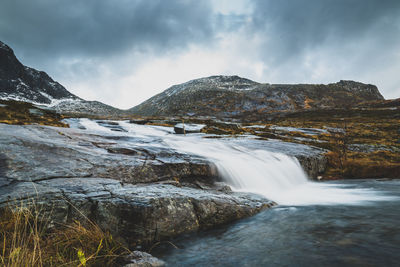 Scenic view of waterfall against cloudy sky