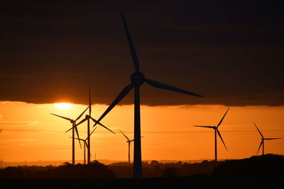 Silhouette wind turbines on field against sky during sunset